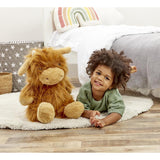 Child lying on a rug with a fluffy brown highland cow soft toy in a cozy bedroom setting