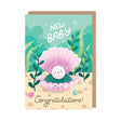 A cute illustrated baby shower card with a kraft envelope behind it. The card shows a smiling pearl in an open pink clam shell underwater, with the words “NEW BABY” at the top and “Congratulations!” at the bottom.