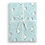A Patterned blue gift wrap present with white storks holding a blue bundle and blue leaves with purple flowers wrapped with white satin ribbon