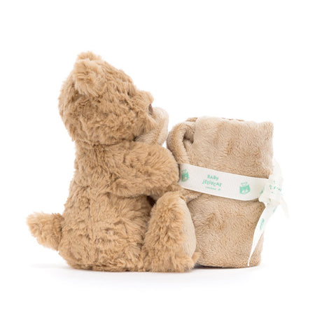 A plush toy bear holding a square-shaped soother, with a ribbon bow and a name tag attached to the soother.