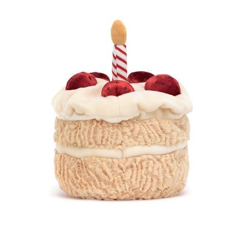 A plush toy resembling a birthday cake, decorated strawberries and with a red and white candle
