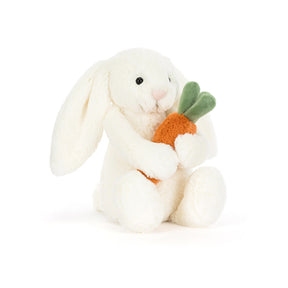 A plush toy of a white bunny holding a carrot with green leaves.
