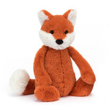 A plush toy depicting a fox cub with fluffy white ears, feet, and tail-tip, sitting with a reddish-brown body.