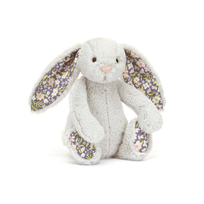 A small plush toy resembling a gray bunny with floral patterns on its ears and feet, and a white backdrop.