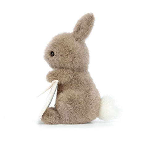 A plush toy resembling a gray bunny holding a beige envelope with a card. side view