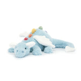 A plush toy resembling a sky blue dragon with rainbow-colored spines, cloud-white wings, and a snout. The dragon is in a lying pose with a serene expression.
