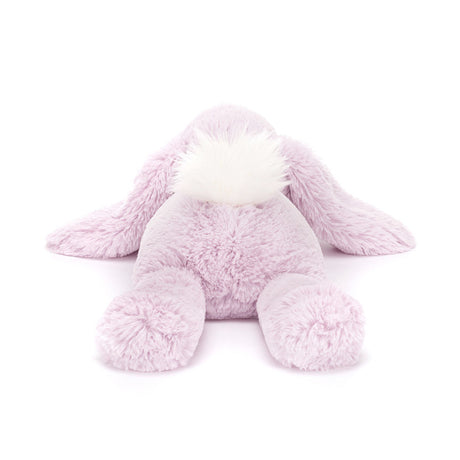 A plush lavender-colored Jellycat Bashful Beige Bunny with a fluffy cream bobtail, lying down.