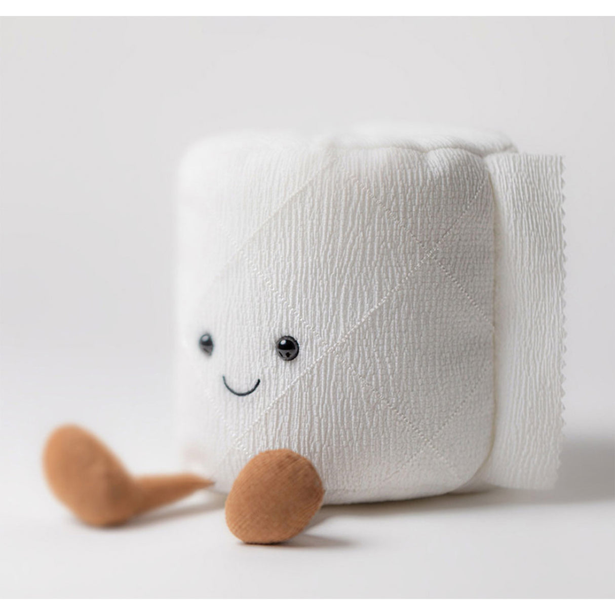 White plush toilet roll with a smiling face and brown feet on a light grey background