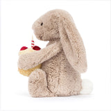 A beige plush toy rabbit sitting upright holding a birthday cake with a single candle on top.