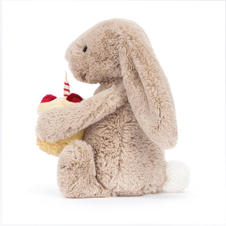 A beige plush toy rabbit sitting upright holding a birthday cake with a single candle on top.