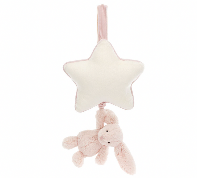 A plush blush pink bunny hanging from a star-shaped musical pull with a cream ribbon.