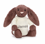 A beige plush toy in the shape of a bunny with long ears, wearing a white jumper with the name 'James' embroidered on the back.