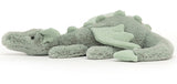 A soft toy depicting a sage green dragon with soft fur, sparkly wings, and a long tail.