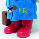 Blue coat with 'P.B.' embroidery, red boots, and a brown bag on a white background