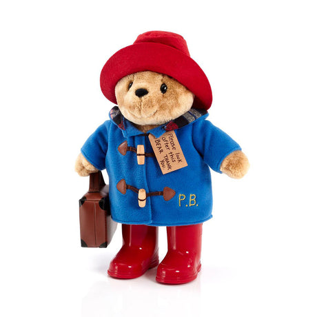 Paddington Plush toy bear in a blue coat, red boots, and red hat with a suitcase on a white background