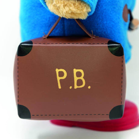 Small brown suitcase with 'P.B.' on it held by a teddy in blue coat.