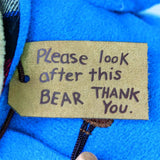 Label on a blue fabric background with text 'Please look after this BEAR THANK YOU'.