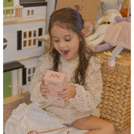 Child holding a pink box with a toy house and other toys in the background