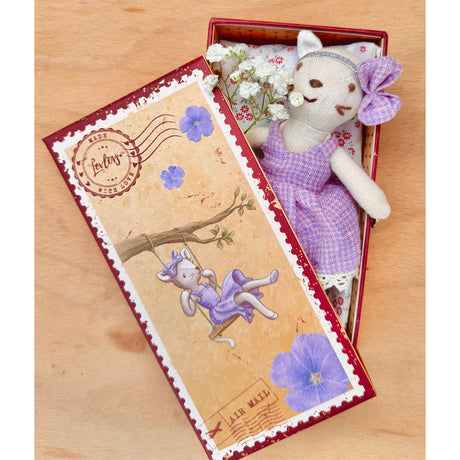 Stuffed cat toy in a box with a decorative card on a wooden surface