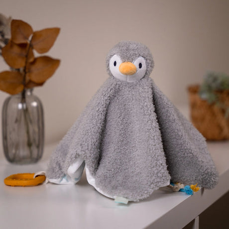 A gray plush penguin baby lovey blanket with a textured fleece-like fabric, featuring a white face and orange beak
