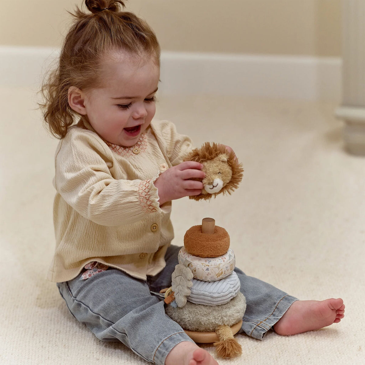 Child playing with little dutch lion stacking toy on a light-colored floor.