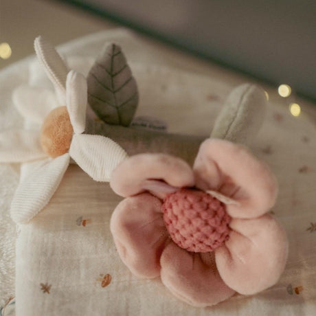 Little dutch Floral-shaped baby rattle toy with pink petals and brown center on a soft fabric background