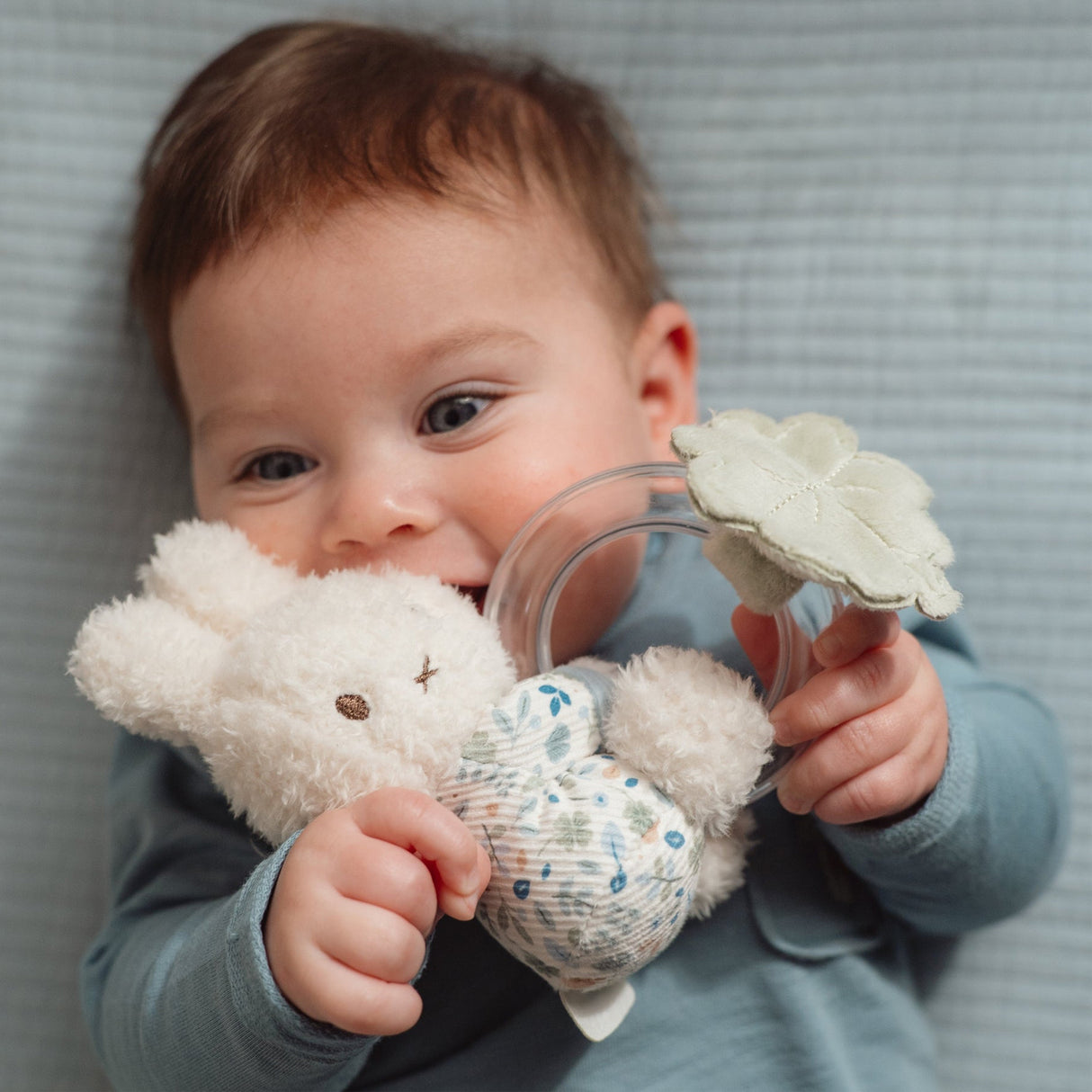 Baby holding a soft Miffy toy rattle with Little Dutch Lucky print clothing and a ring rattle with tiny beads and a soft leaf 