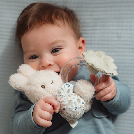 Baby holding a soft Miffy toy rattle with Little Dutch Lucky print clothing and a ring rattle with tiny beads and a soft leaf 