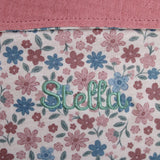Floral patterned fabric with name embroidered in green thread on a pink background