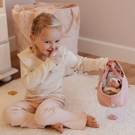 Child playing with a baby doll in a pink basket on a carpeted floor.