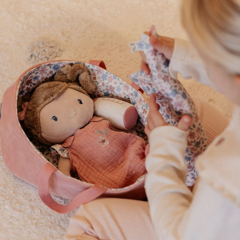 Child playing with a doll in a floral carry cot on a soft surface