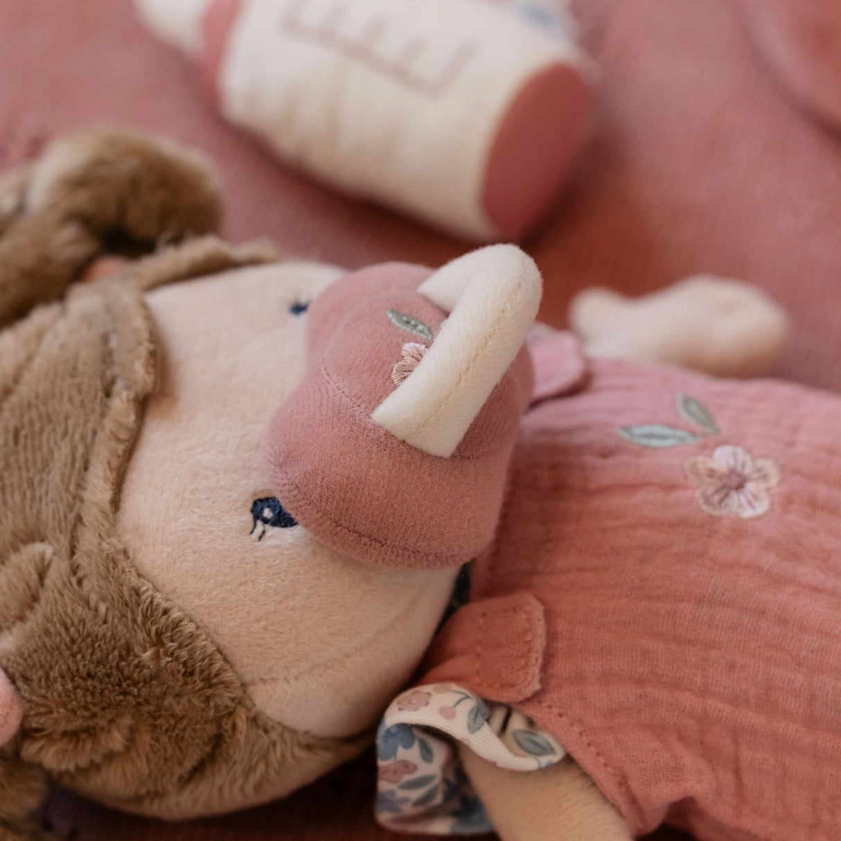 Close-up of a plush toy with a pink dummy and floral dress, held by a person.