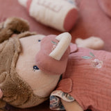Close-up of a plush toy with a pink dummy and floral dress, held by a person.