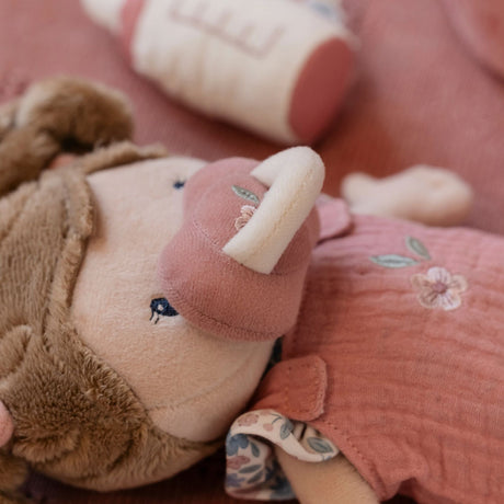 Close-up of a plush toy with a pink dummy and floral dress, held by a person.