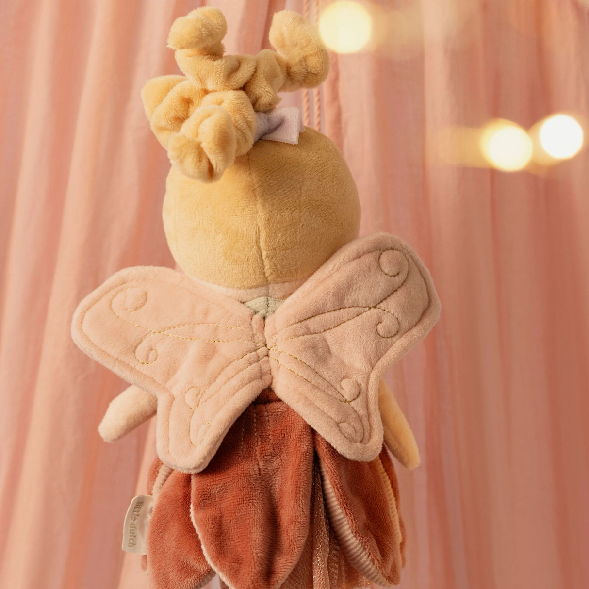 Back view of Little Dutch Fairy Mila doll showing detailed embroidered fairy wings against a pink backdrop