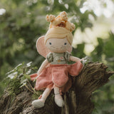 Little Dutch Fairy Mila cuddle doll sitting on a mossy tree trunk in a garden setting