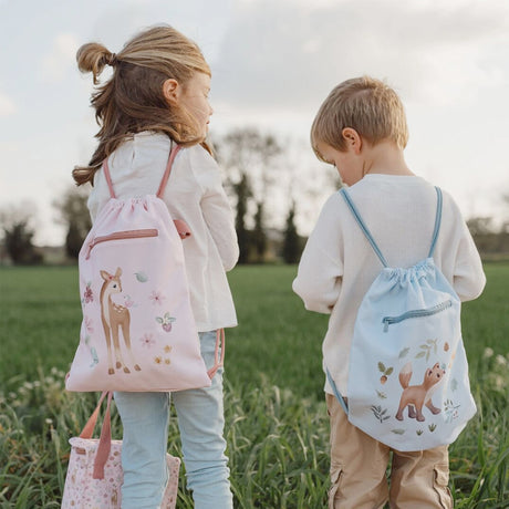 Two children standing in a field with Little Dutch drawstring bags featuring animal designs.
