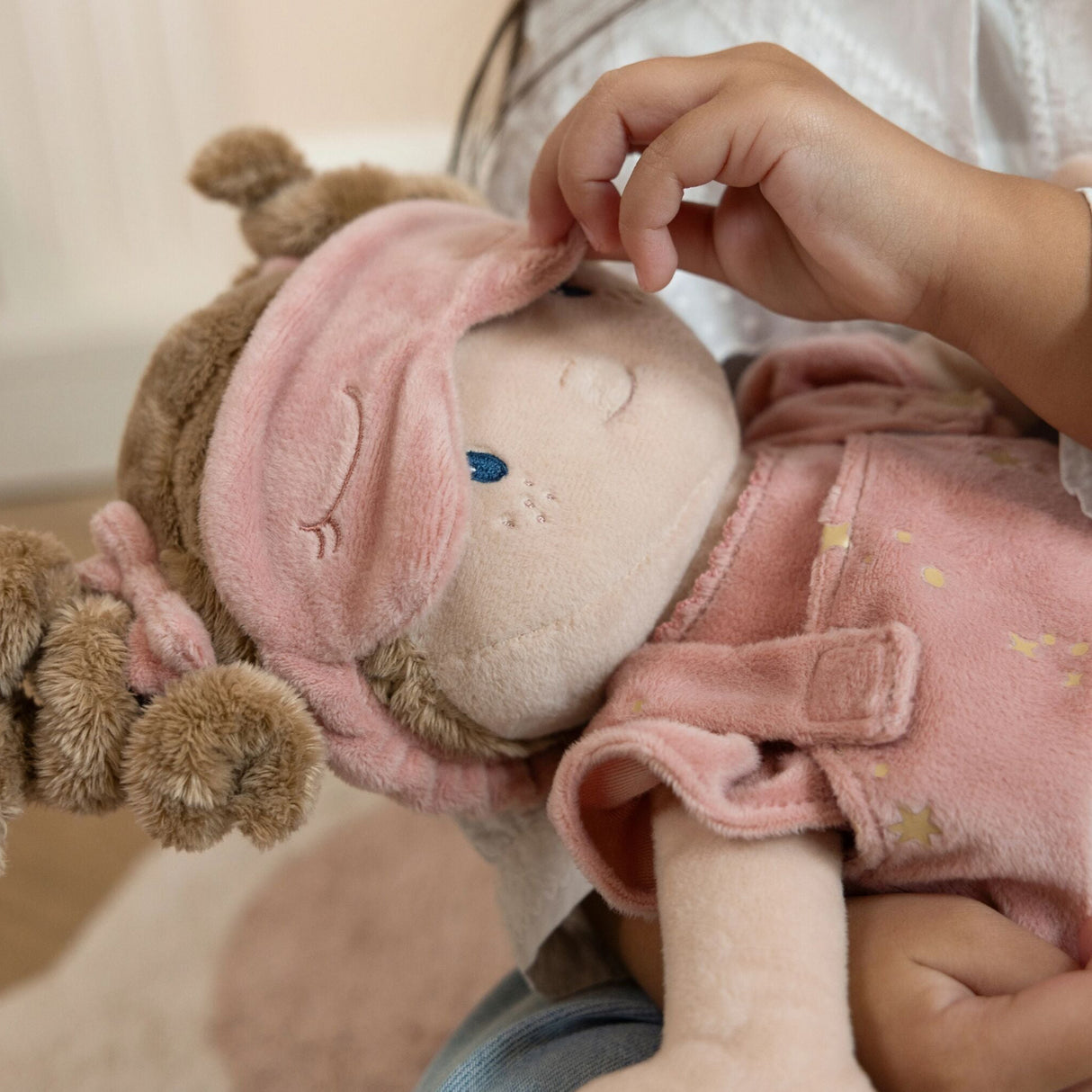 Child holding a soft tbaby doll with a pink outfit and headband.