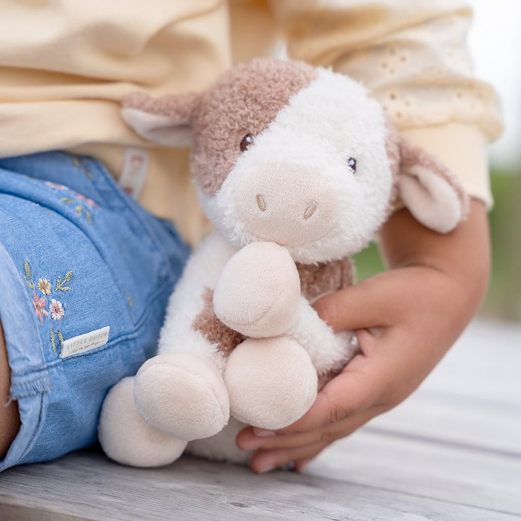 Child holding a Little Duth  plush toy in their lap with a blurred background