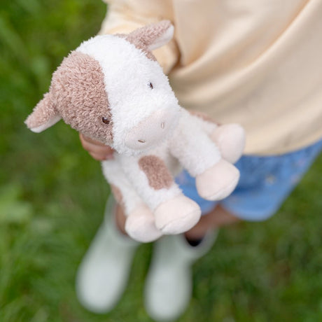 Child holding a small brown and white plush Cow toy outdoors.