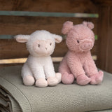 Stuffed lamb and pig toy sitting on a textured surface with a wooden background