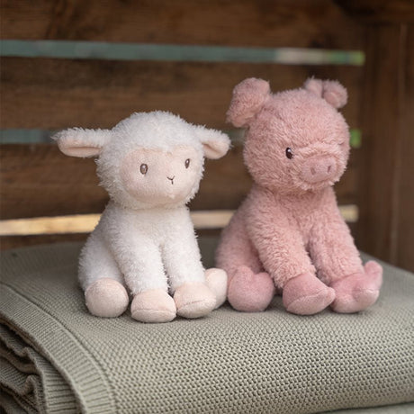 Stuffed lamb and pig toy sitting on a textured surface with a wooden background