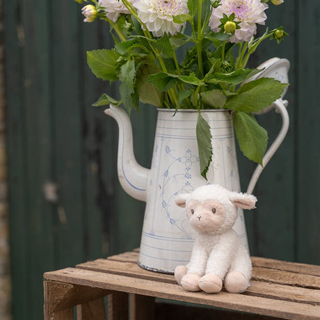 Floral arrangement in a teapot with a plush lamb toy on a wooden surface.