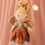 Close-up of Little Dutch Fairy Mila doll face with embroidered features and pink wings against a warm pink backdrop