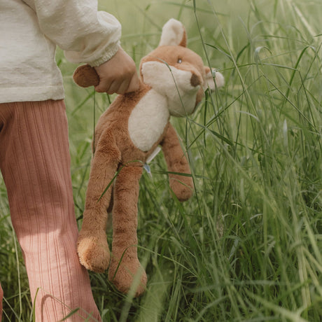 Person holding a plush fox toy in a grassy field