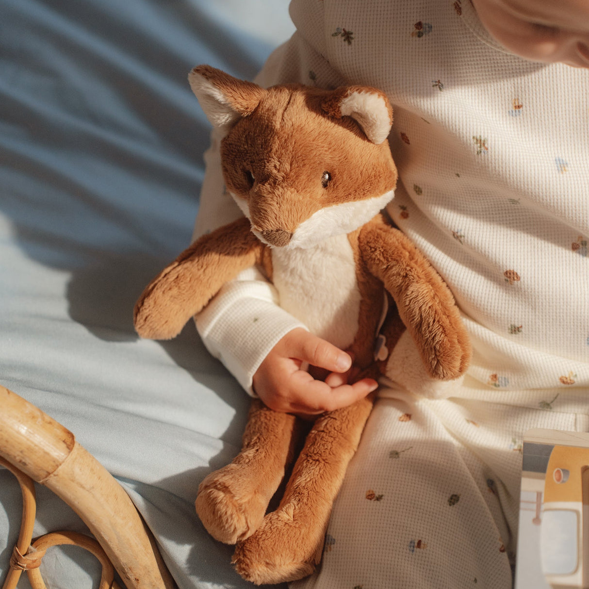 Child holding a plush fox toy on a light blue blanket