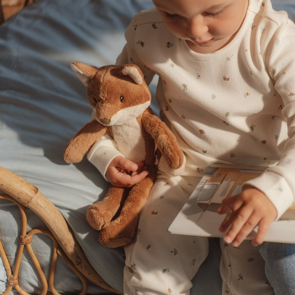 Child holding a soft fox toy and a book on a bed