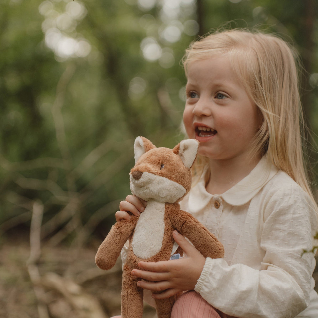 Young girl holding a plush fox toy outdoors with a blurred natural background