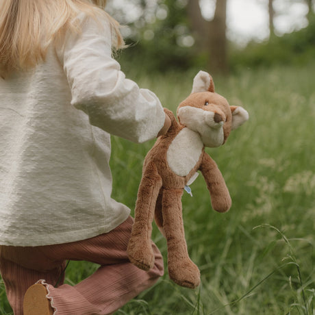Child holding a plush fox toy in a grassy outdoor setting