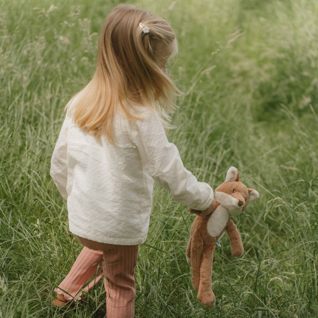 Child holding a plush toy in a grassy field